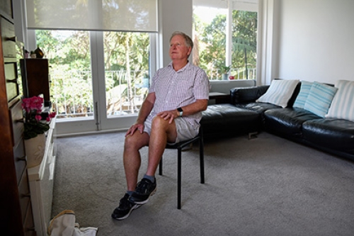 An older man performs seated exercises at home.